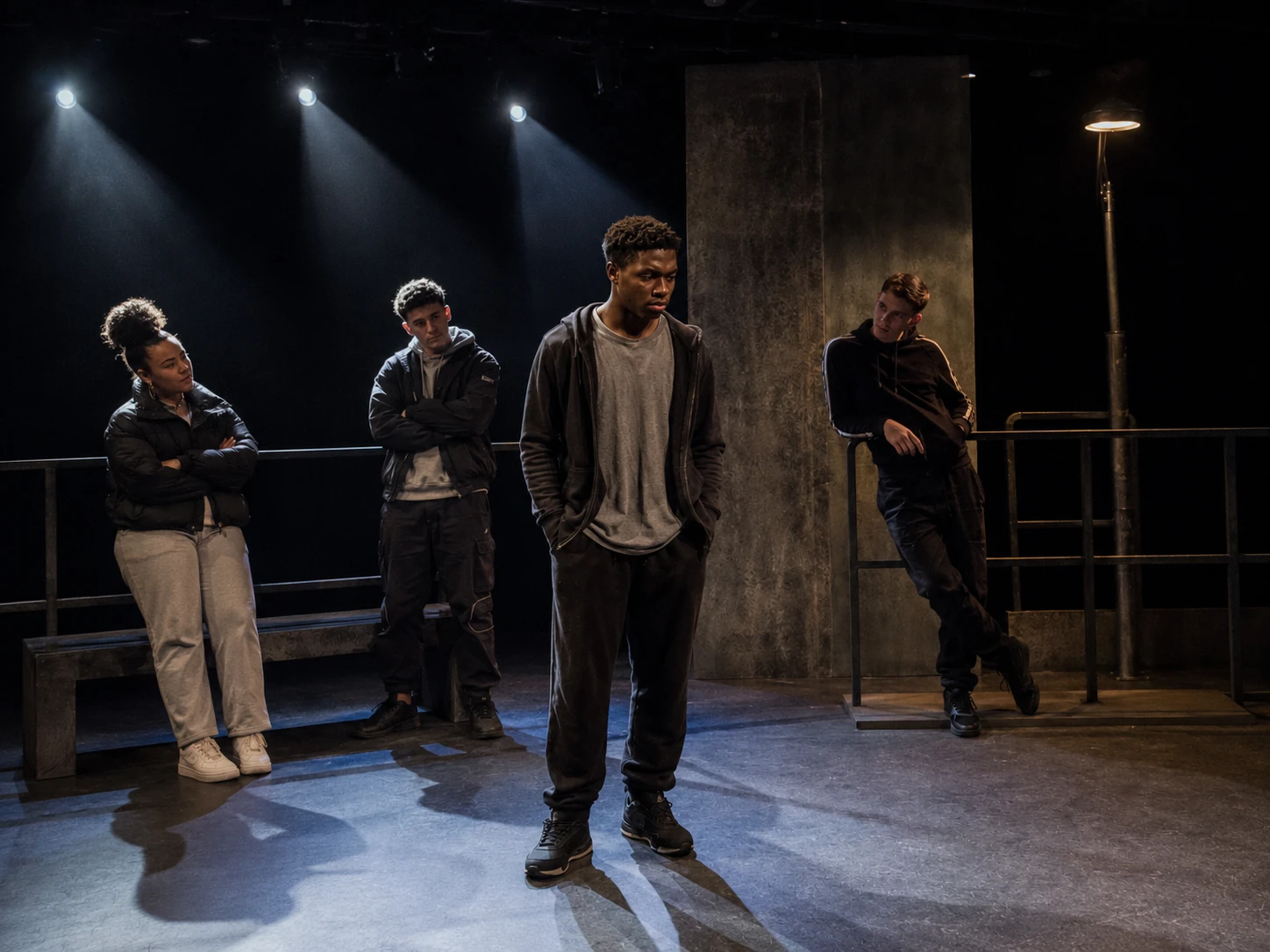 A flexible industrial urban stage for Face with Martin isolated in a pool of light while other characters watch from the edges.