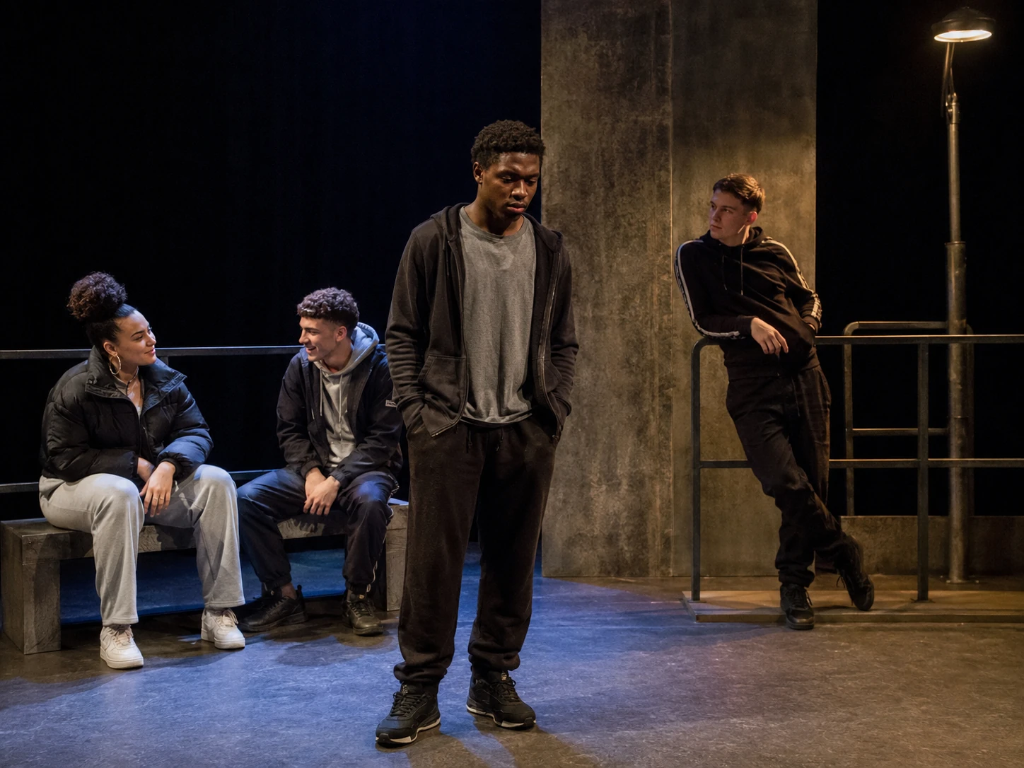 Young adult actors playing the teenage characters in Face on a flexible urban stage, with Martin standing apart from the group.